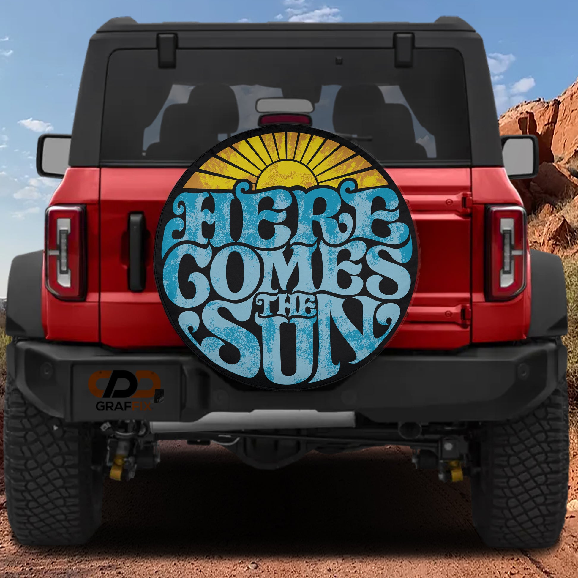 a red Jeep Wrangler with a large sun-shaped decal on the rear window that says "HERE COMES THE SUN".