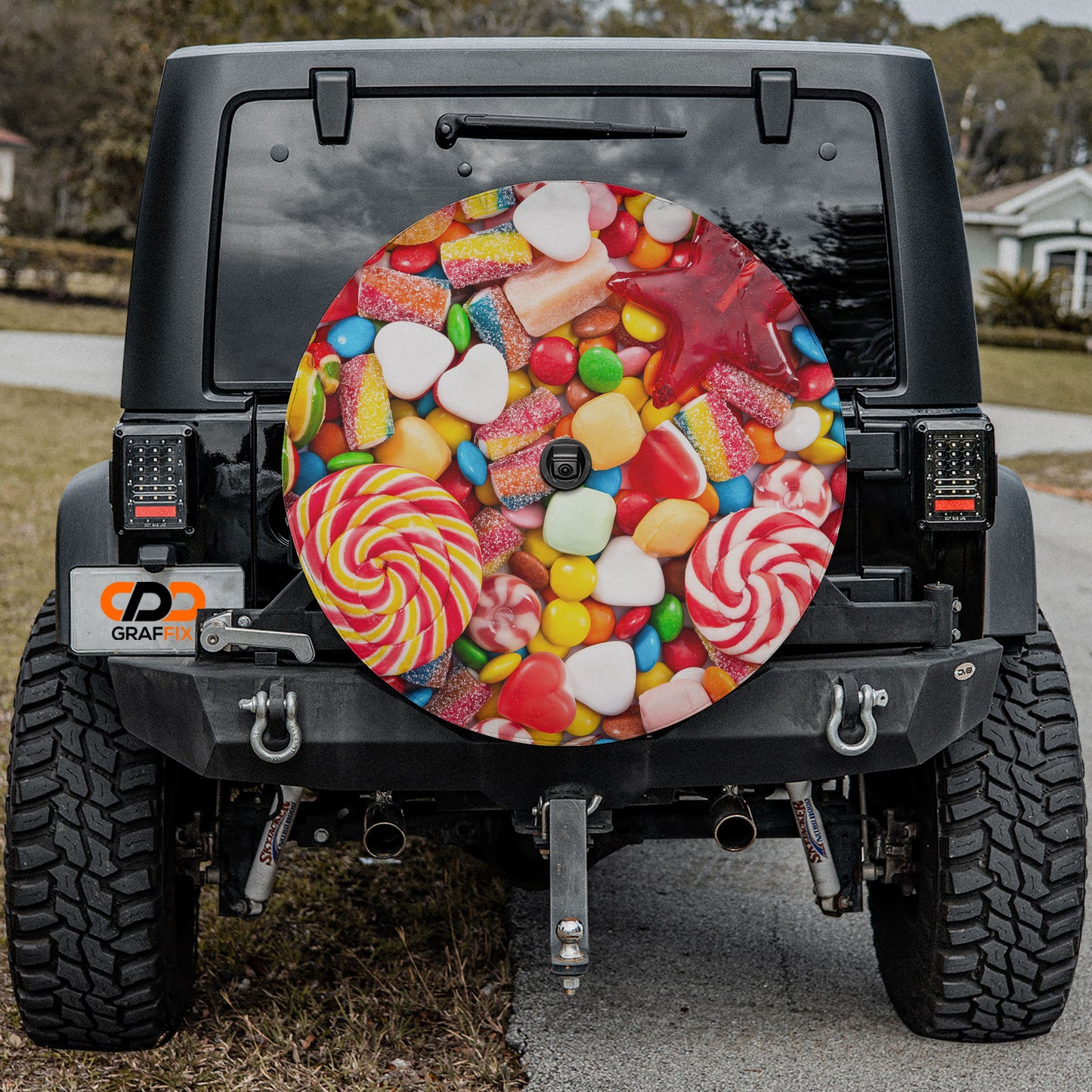a black Jeep Wrangler with a large, colorful wheel cover featuring various candies and sweets attached to the rear of the vehicle.