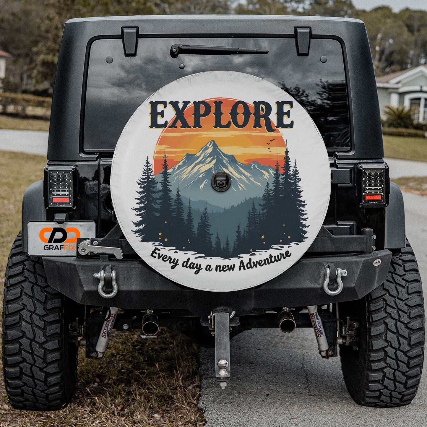 the back of a black Jeep Wrangler with a large wheel cover featuring a mountain landscape and the word "EXPLORE" prominently displayed.