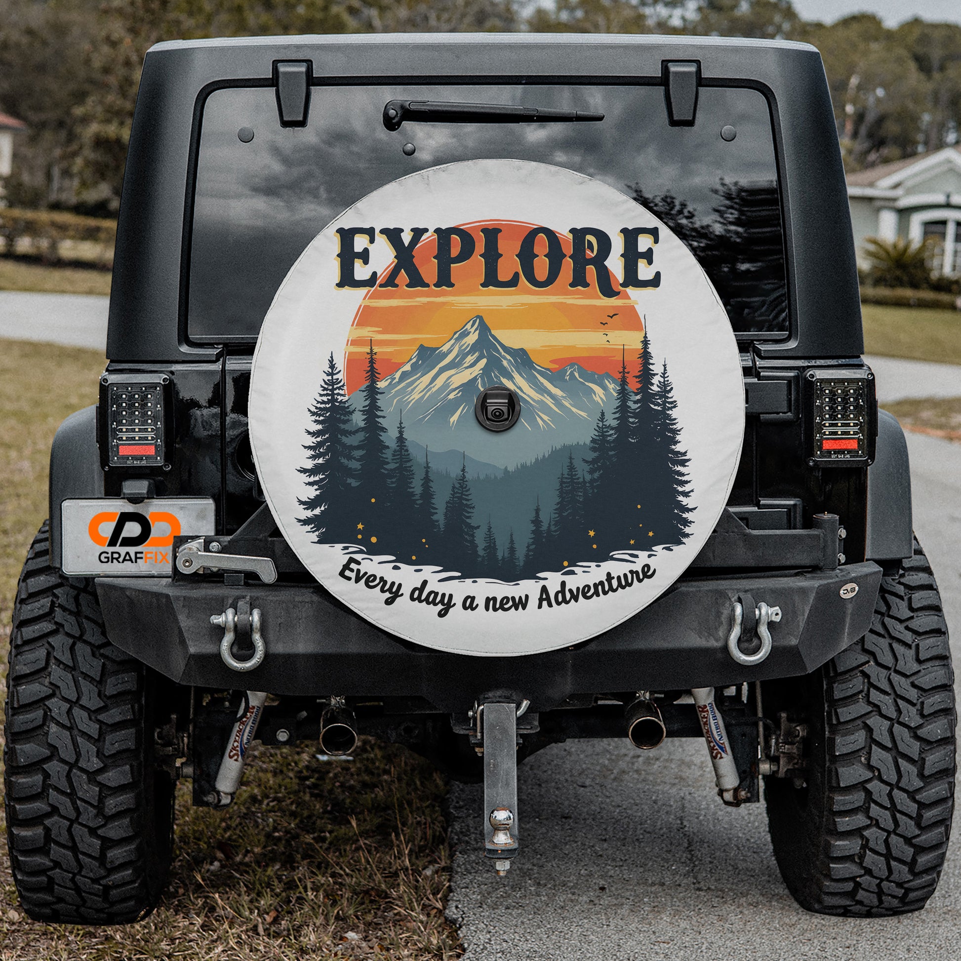 the back of a black Jeep Wrangler with a large wheel cover featuring a mountain landscape and the word "EXPLORE" prominently displayed.