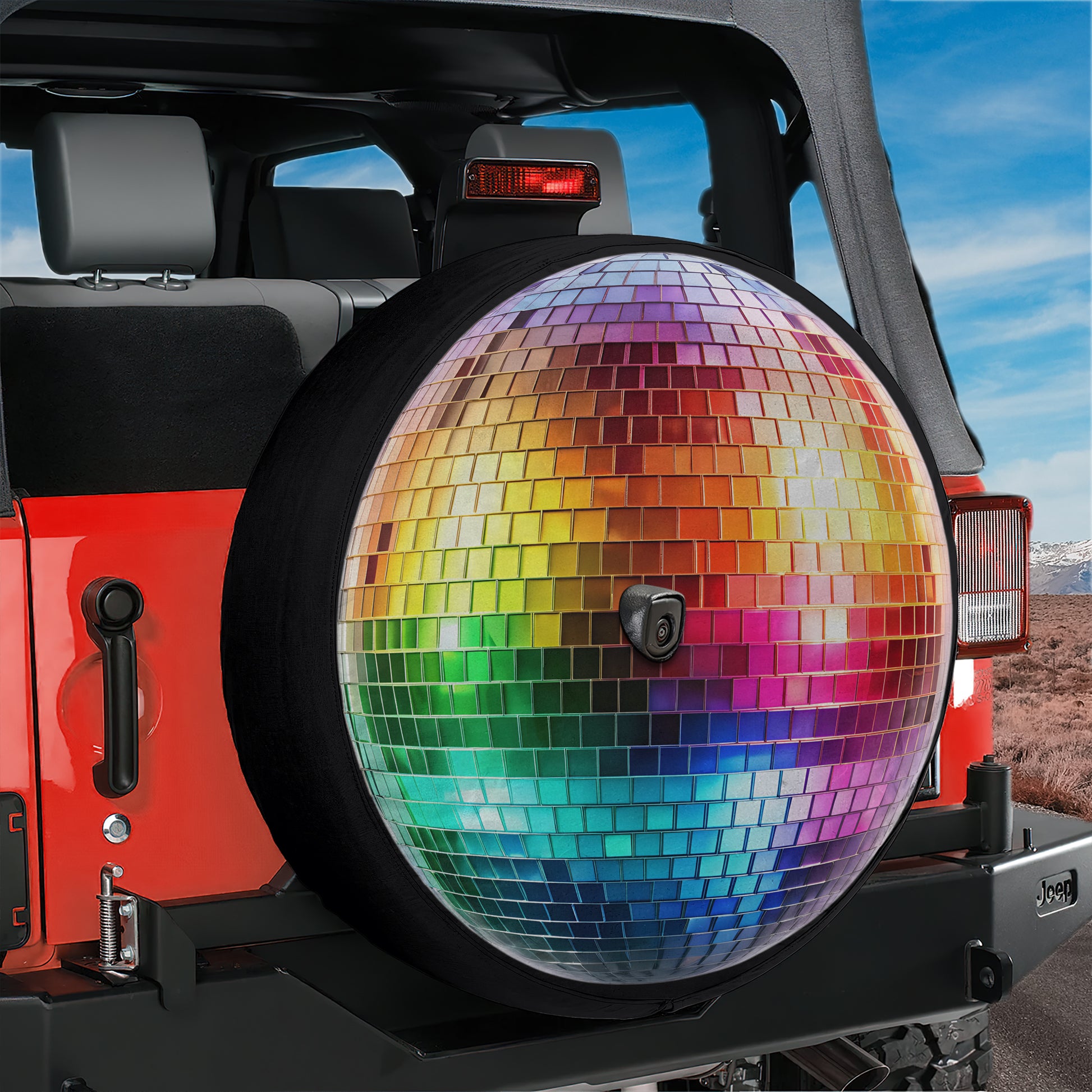 A colorful disco ball-patterned spare tire is attached to the rear of a red Jeep vehicle, with a desert landscape visible in the background.