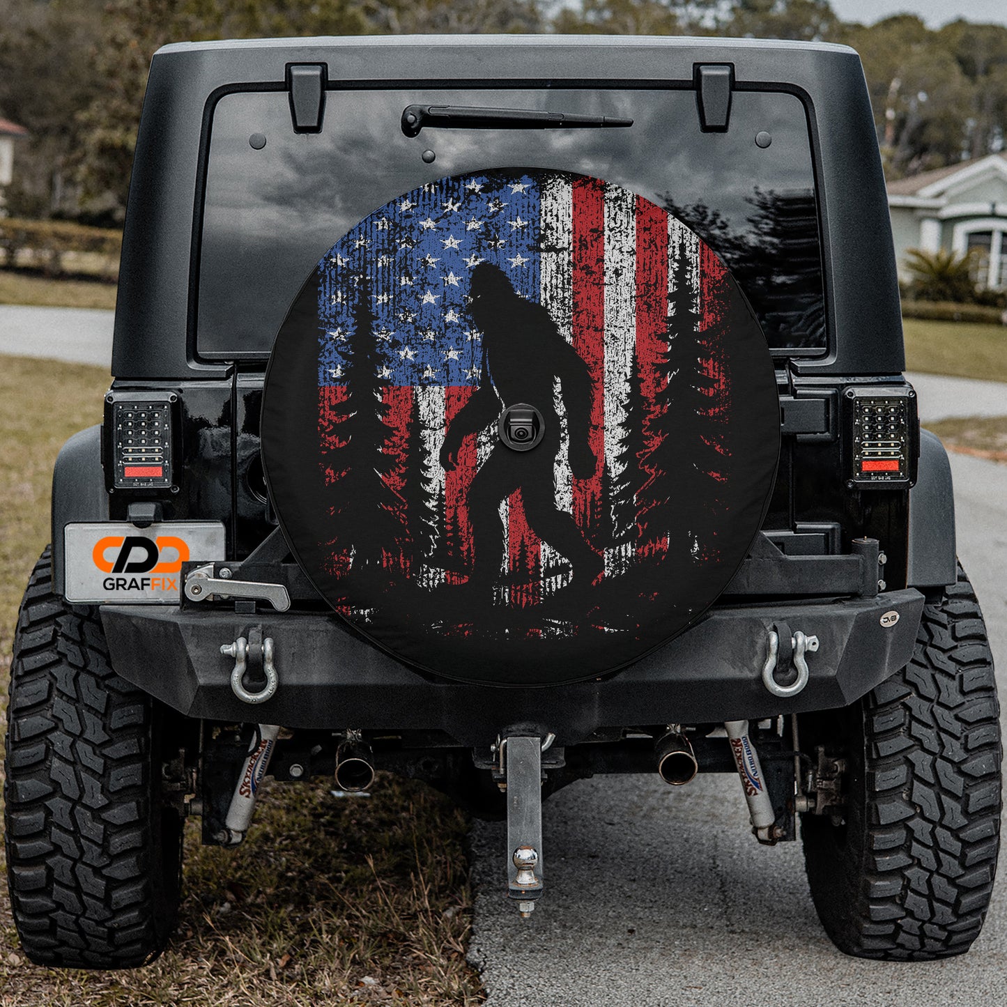 a black Jeep Wrangler with a large American flag-themed spare tire cover on the rear.