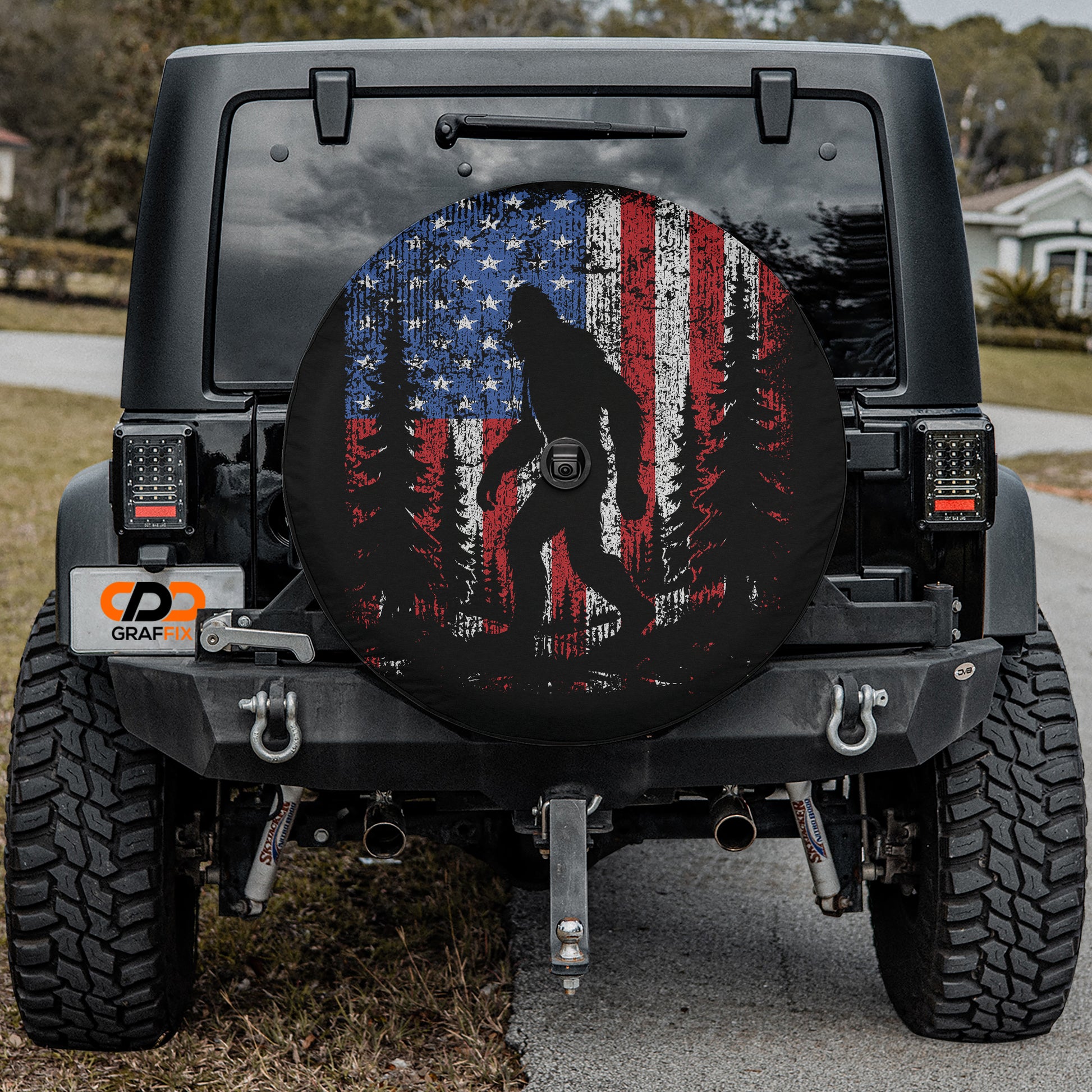 a black Jeep Wrangler with a large American flag-themed spare tire cover on the rear.