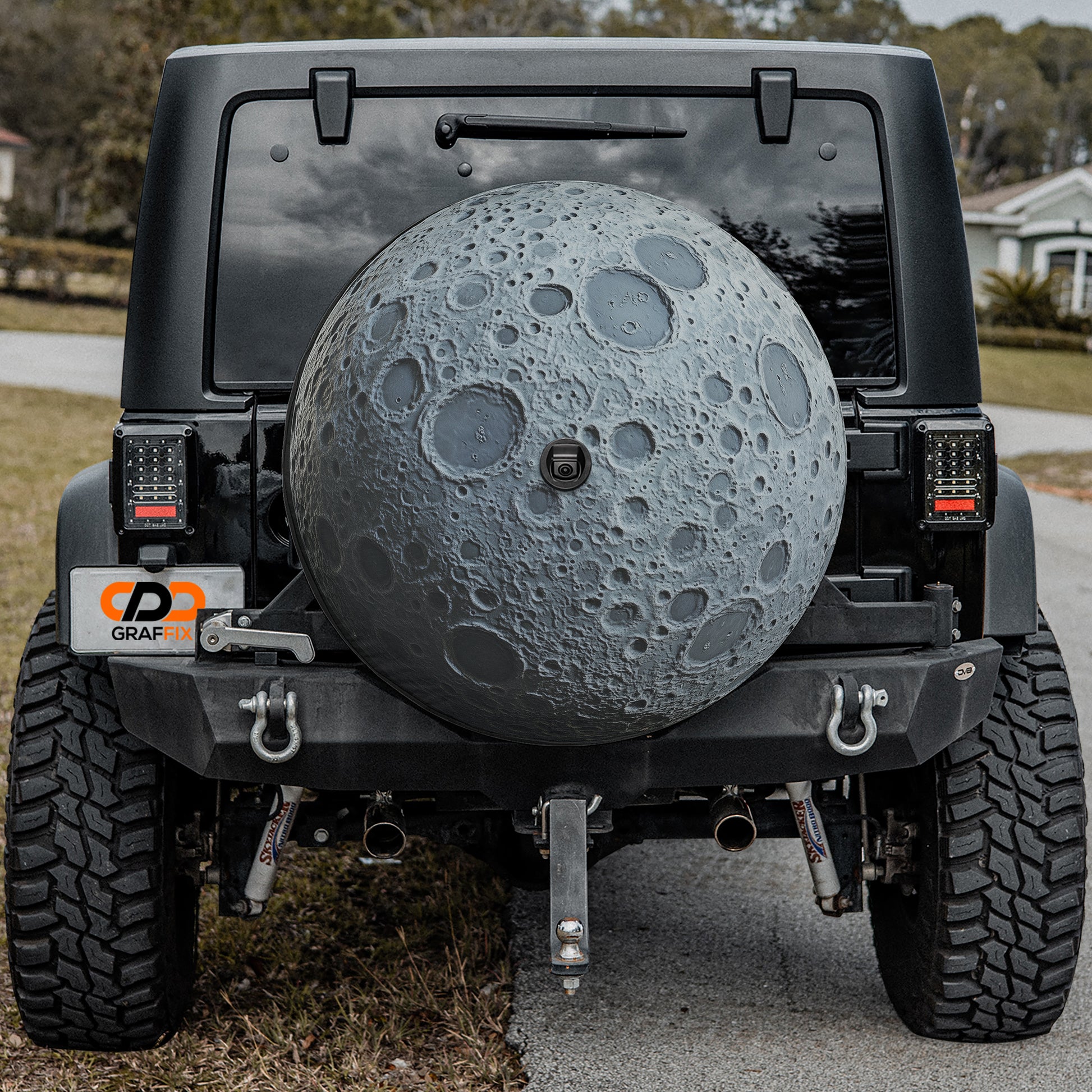 a black Jeep Wrangler with a large, detailed moon-shaped spare tire mounted on the rear of the vehicle.