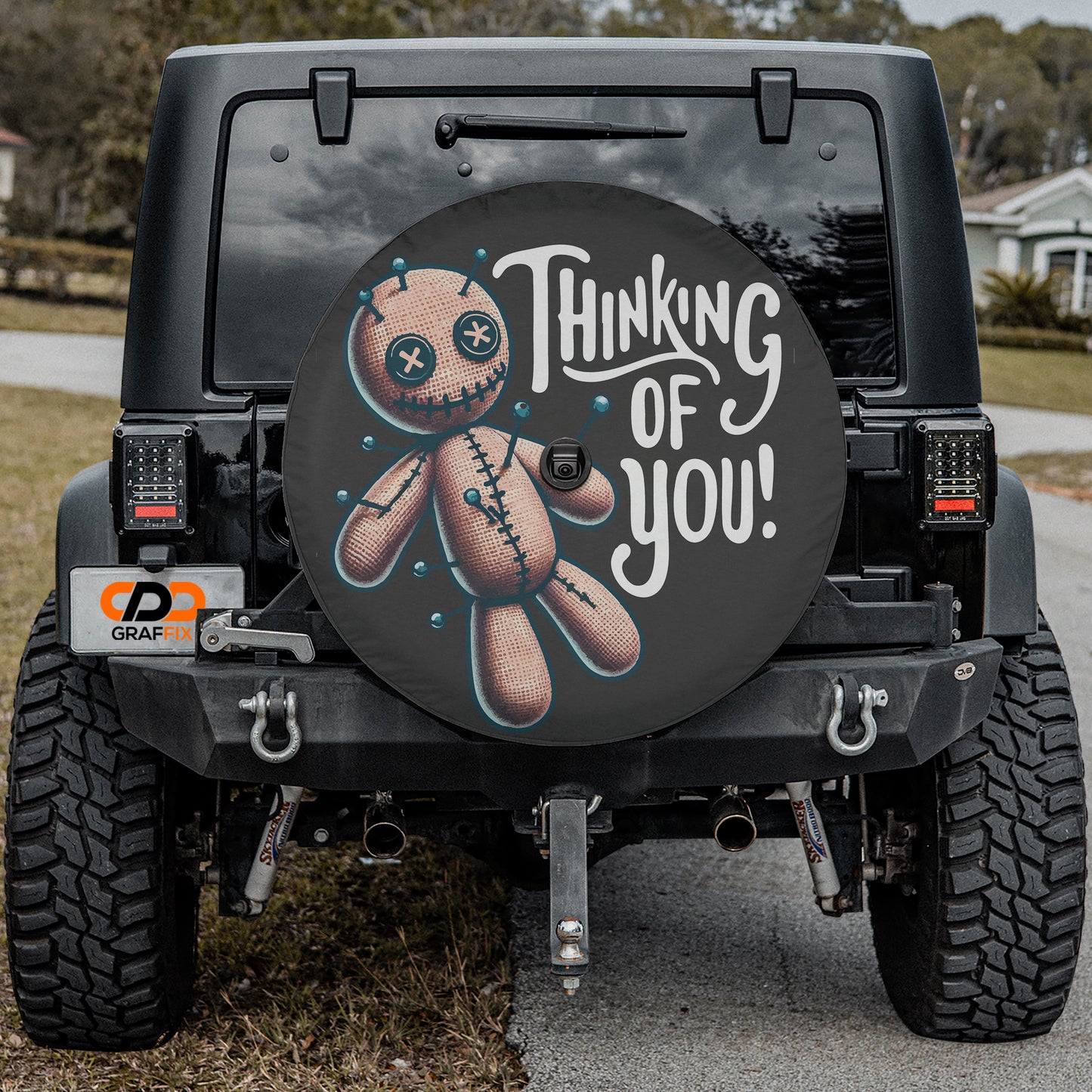 a black jeep with a large tire cover on the rear of the vehicle. The cover has a cartoon character and the text "Thinking of You!" written on it.