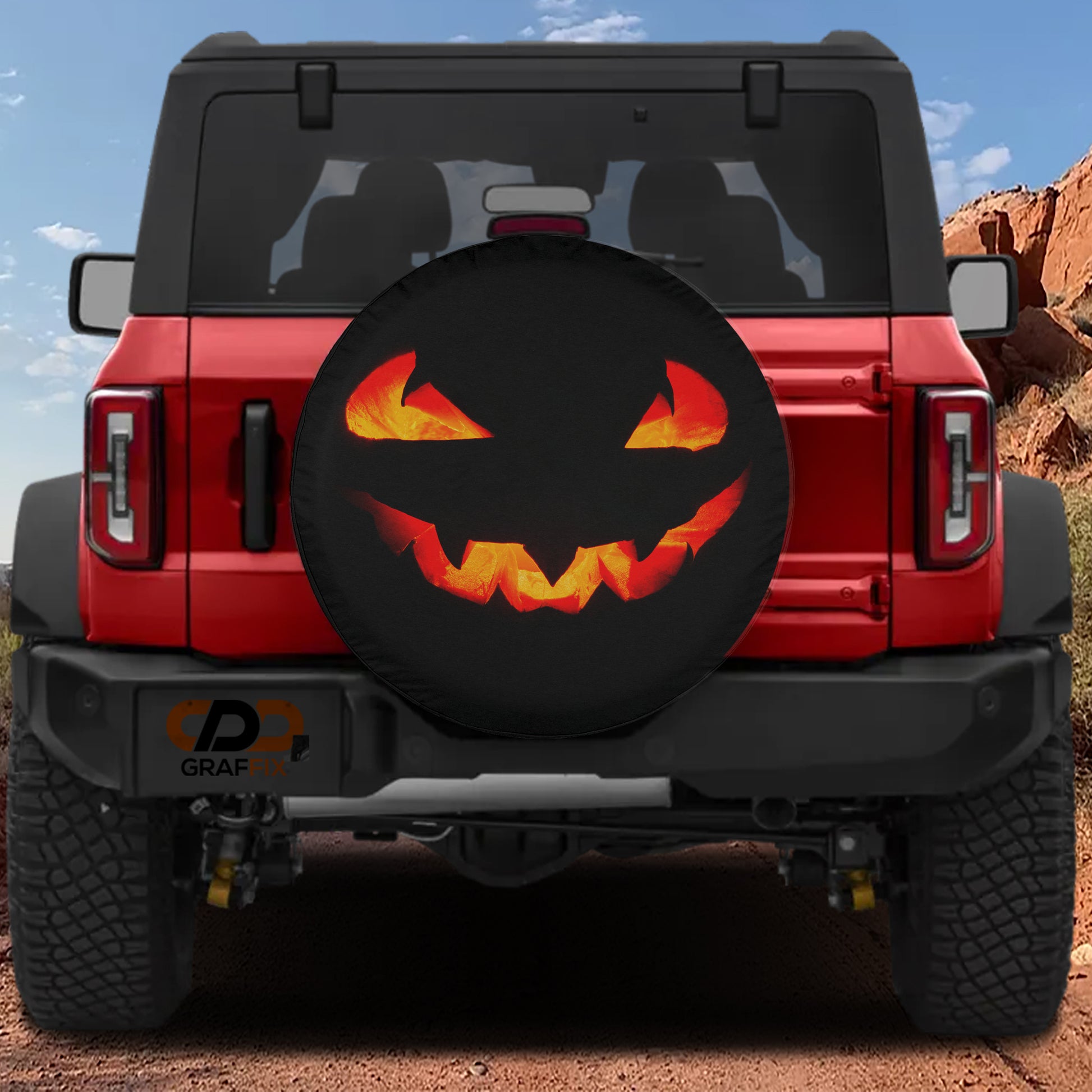 A red Jeep Wrangler with a Halloween-themed spare tire cover featuring a jack-o-lantern design.