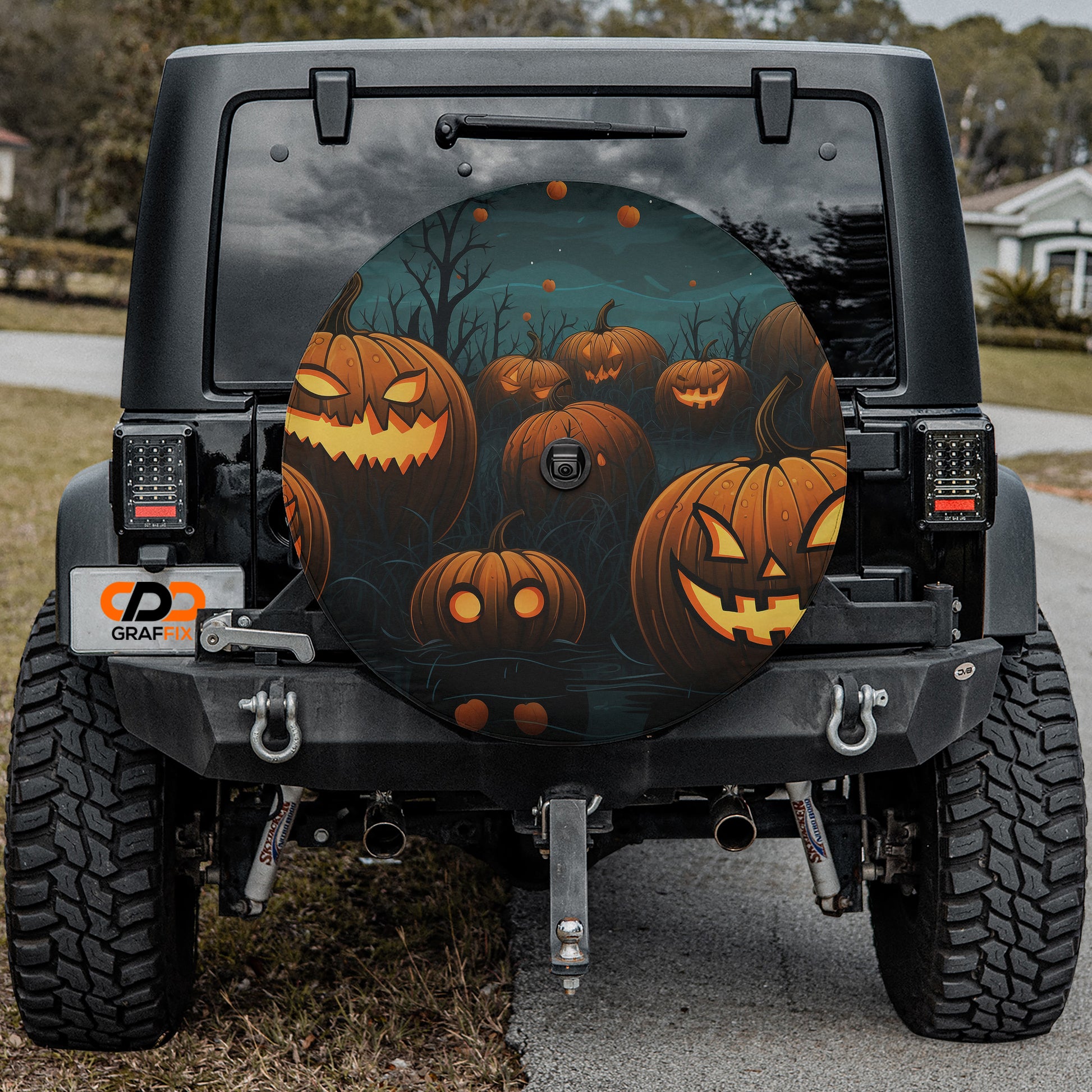 a black Jeep Wrangler with a Halloween-themed spare tire cover featuring jack-o-lanterns and a spooky forest scene.