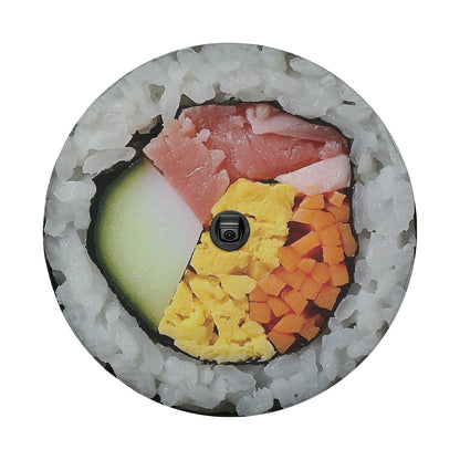 A sushi roll with various ingredients, including rice, meat, vegetables, and a black camera lens, arranged in a circular pattern.