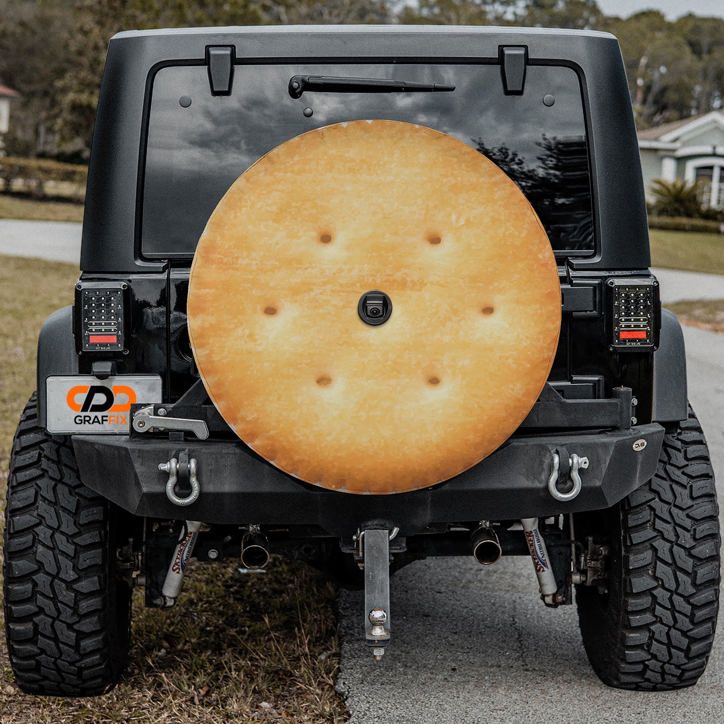 a black Jeep Wrangler with a large, round, yellow-brown cracker attached to the rear of the vehicle.