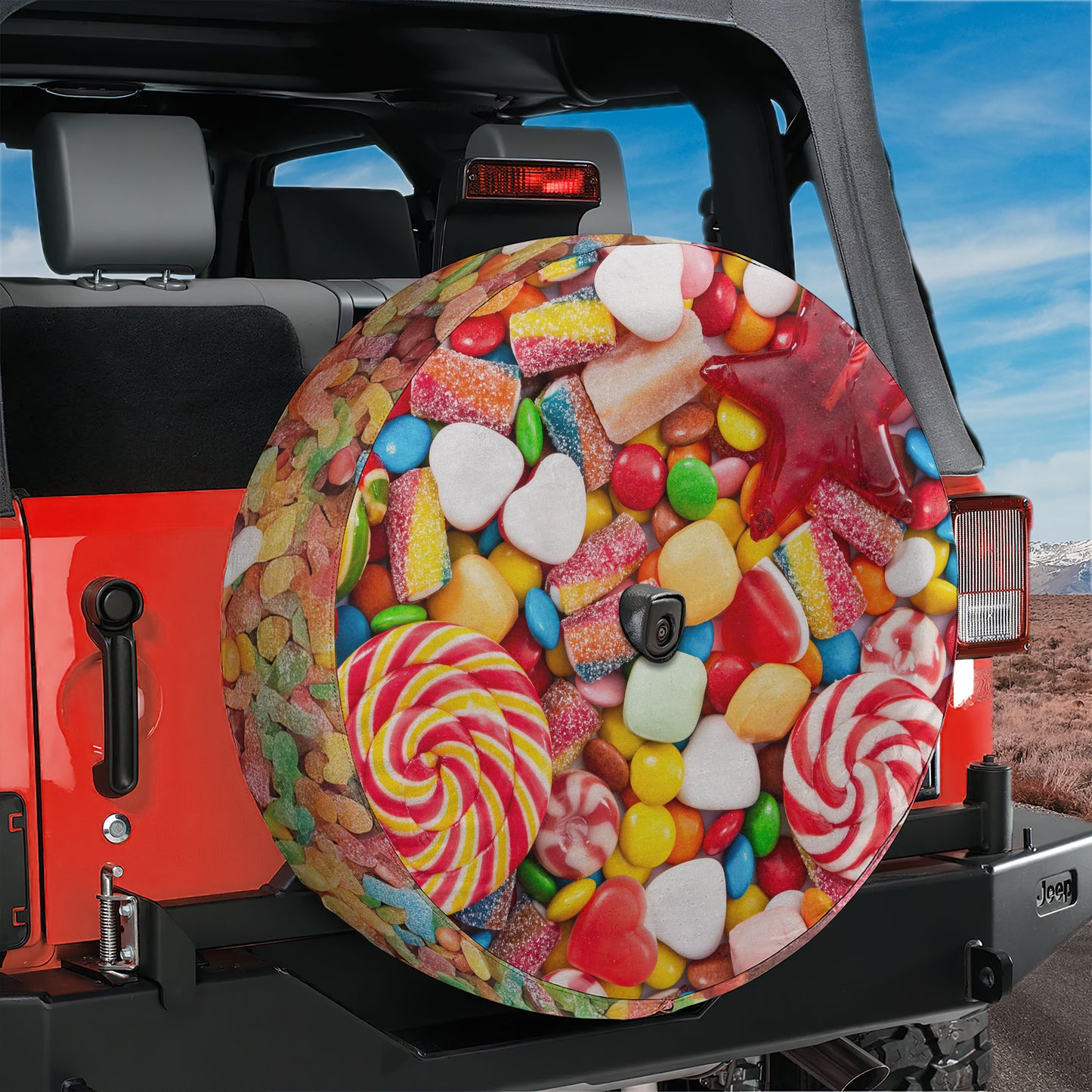 A colorful and vibrant tire cover with various candies and sweets printed on it, attached to the rear of a red Jeep vehicle.