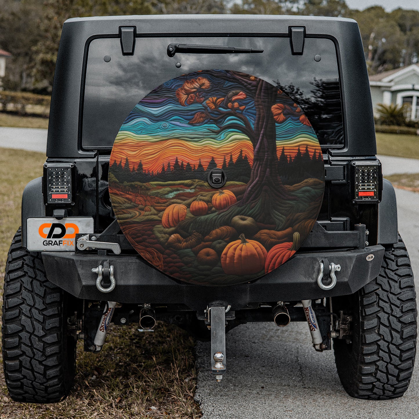 the rear of a black Jeep Wrangler with a large, colorful wheel cover featuring a pumpkin and autumn foliage design.