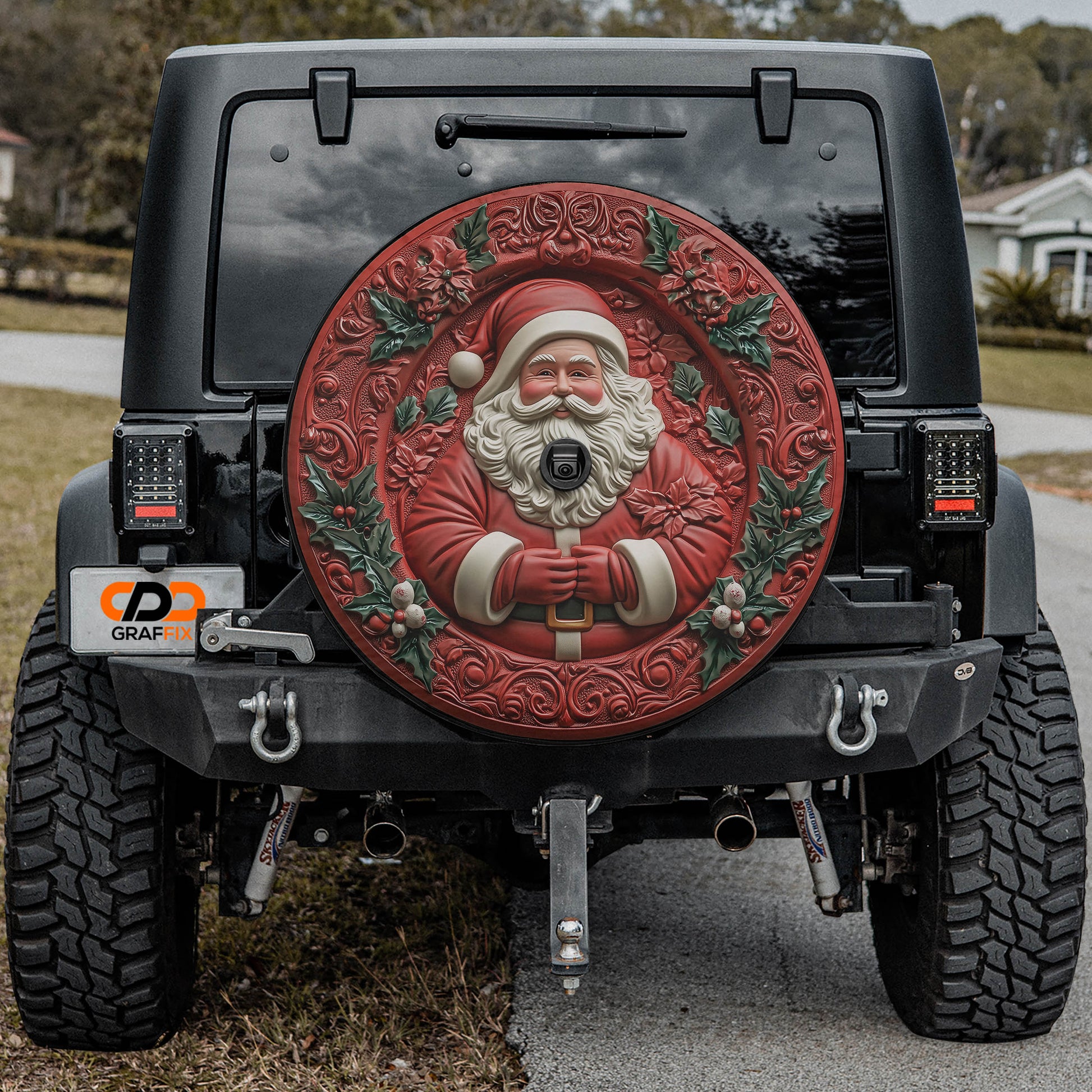 a black Jeep Wrangler with a large, decorative wheel cover featuring a Santa Claus image. The Jeep is parked on a road, and there is a house visible in the background.
